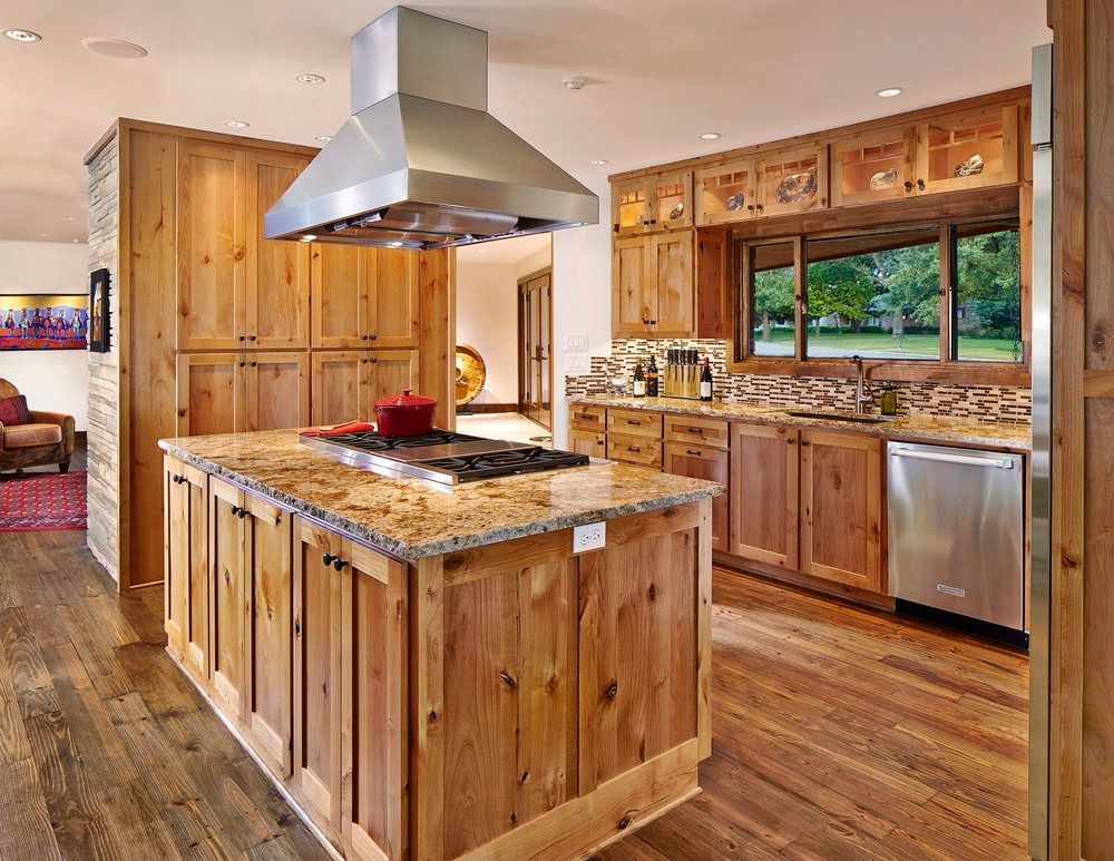 Rustic kitchen with wood cabinets, island, and granite countertops. Stainless steel appliances and range hood.