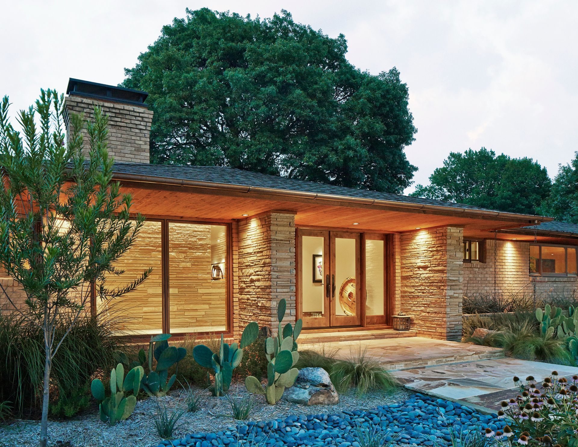 Modern home exterior with stone facade, large windows, and landscaped yard.
