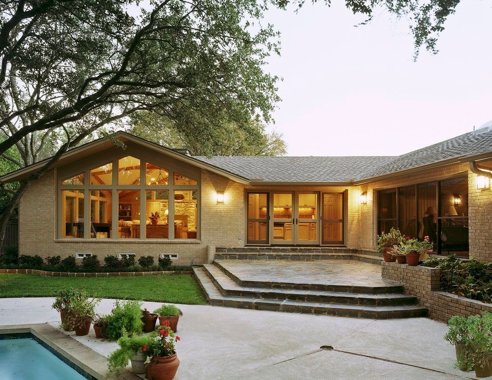Brick house exterior with large windows, patio, pool, and greenery.