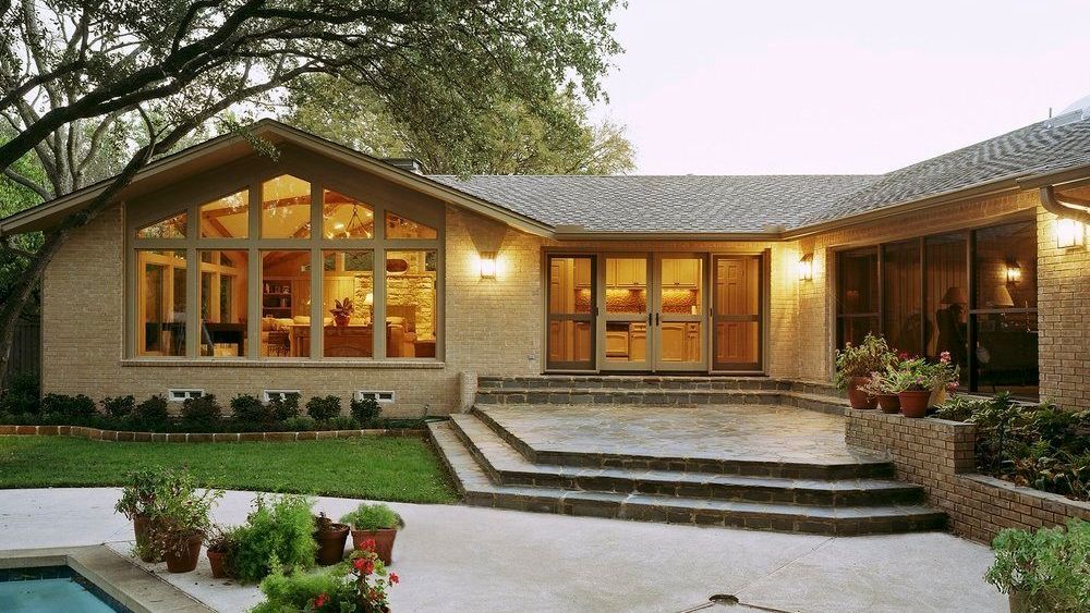 Stone-clad house exterior with large windows, steps leading to a patio, and a swimming pool.