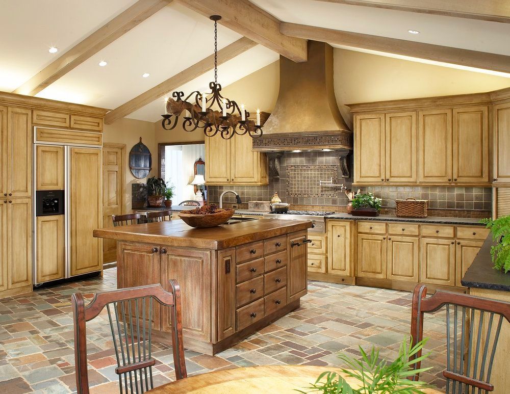 Rustic kitchen with wooden cabinets, island, stone floor, and chandelier.
