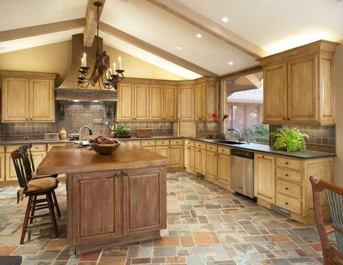 Rustic kitchen with light wood cabinets, stone tile floor, and island.