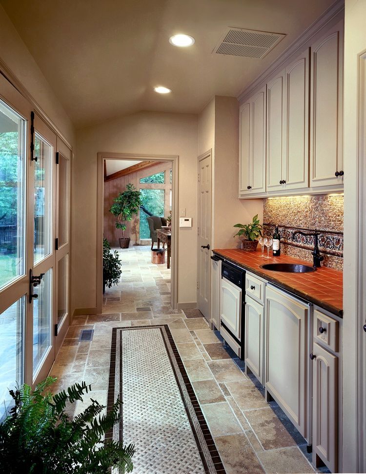 Long, narrow kitchen with beige cabinets, red countertop, and mosaic tile floor. Door to patio.
