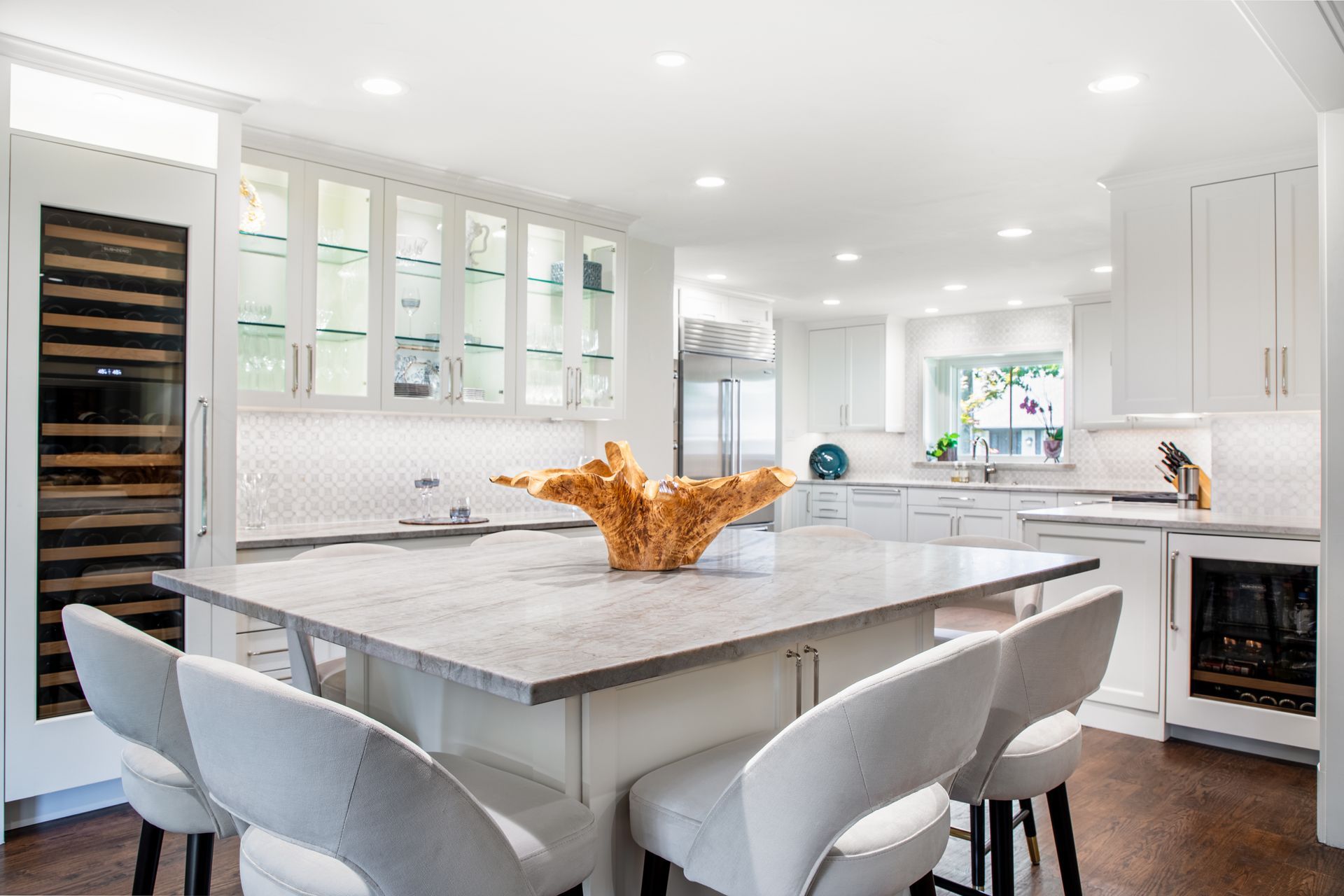 Bright, white modern kitchen with island, seating, and decorative coral. Cabinets, appliances, and recessed lighting.