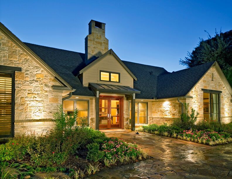 Stone house exterior illuminated at dusk with landscaped yard and driveway. Highland Park exterior renovation.