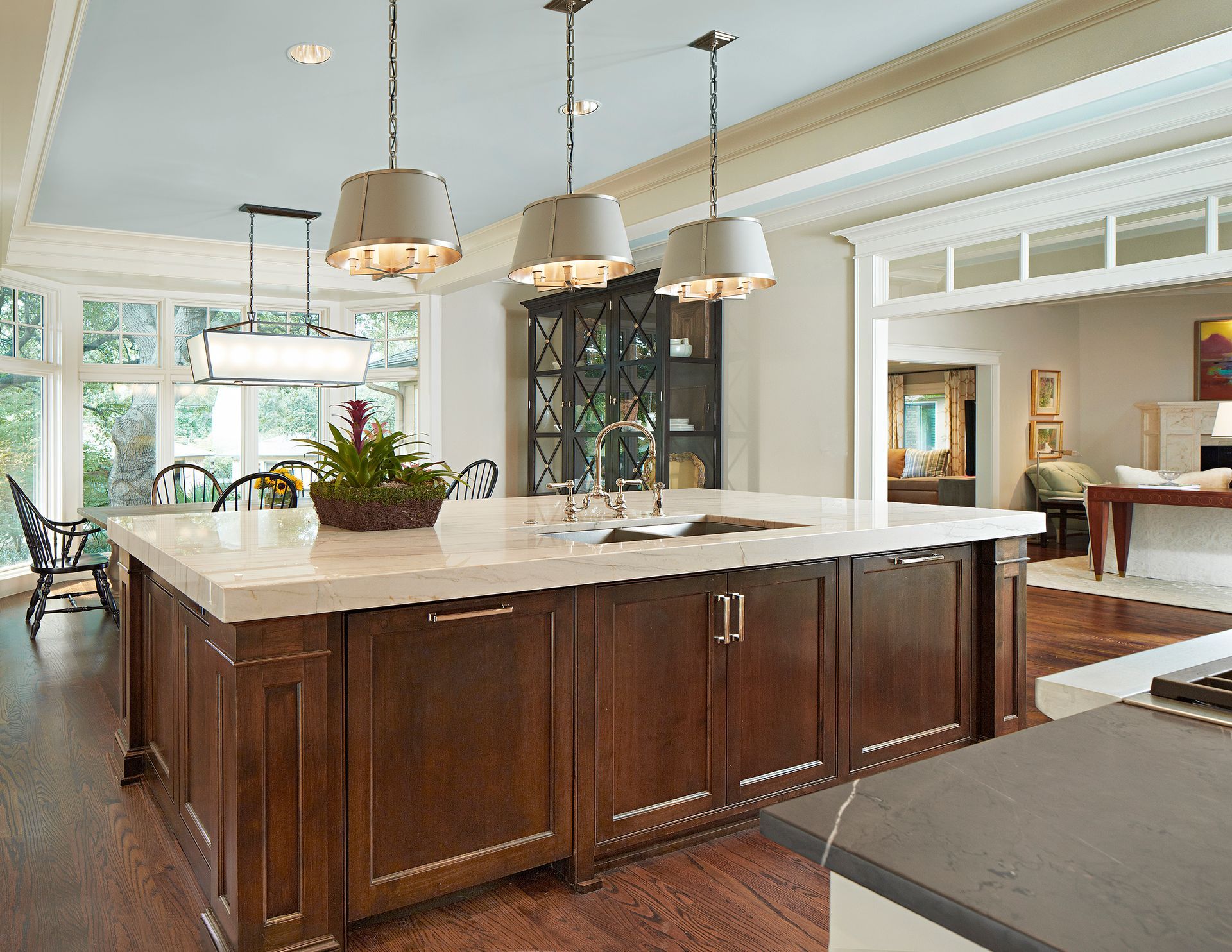 Kitchen island with dark wood cabinets, light countertop, pendant lights, and view of dining area.