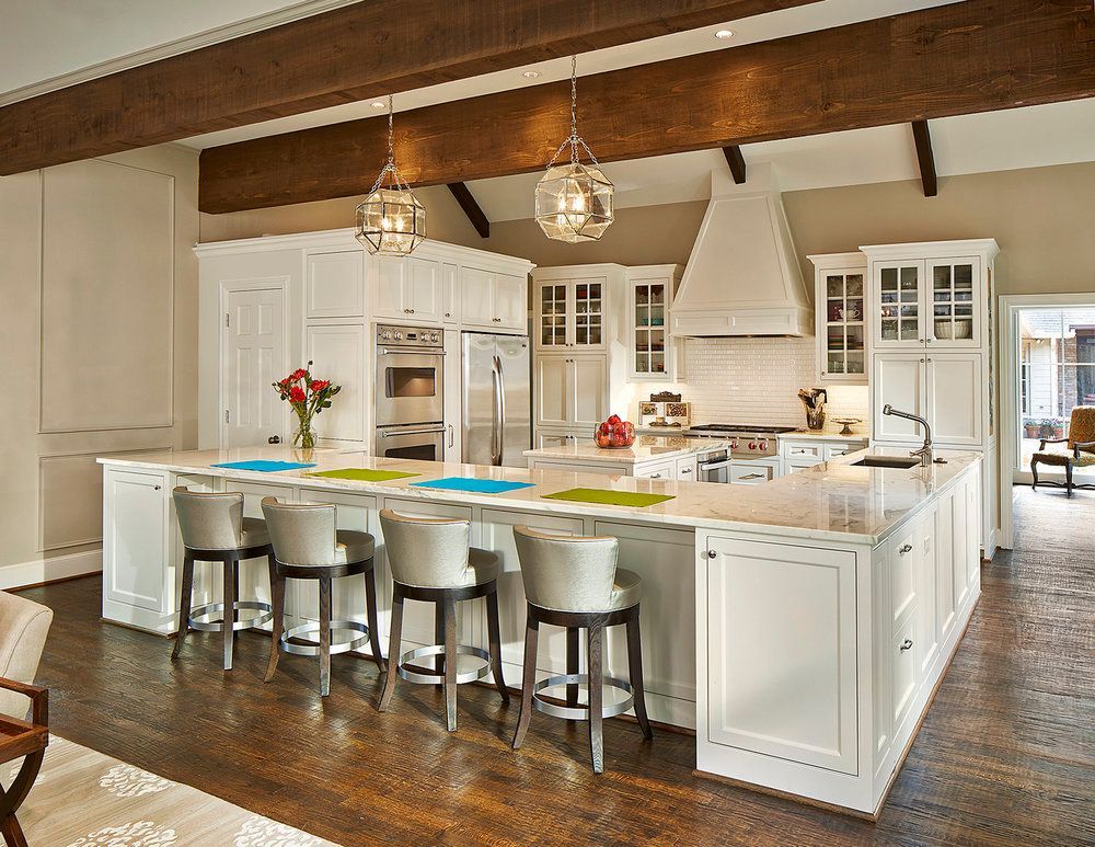 White kitchen with large island, seating, and decorative pendant lights. Dark wood floors and exposed beams.