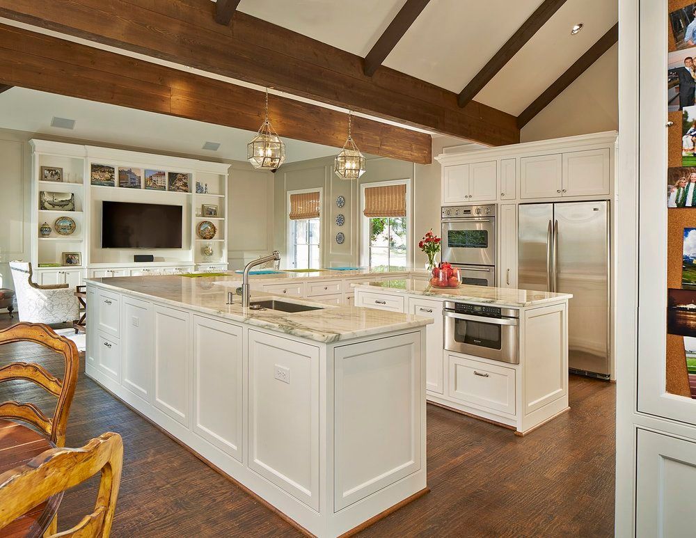 Spacious kitchen with white cabinetry, granite countertops, and dark wooden beams. Stainless steel appliances and island.