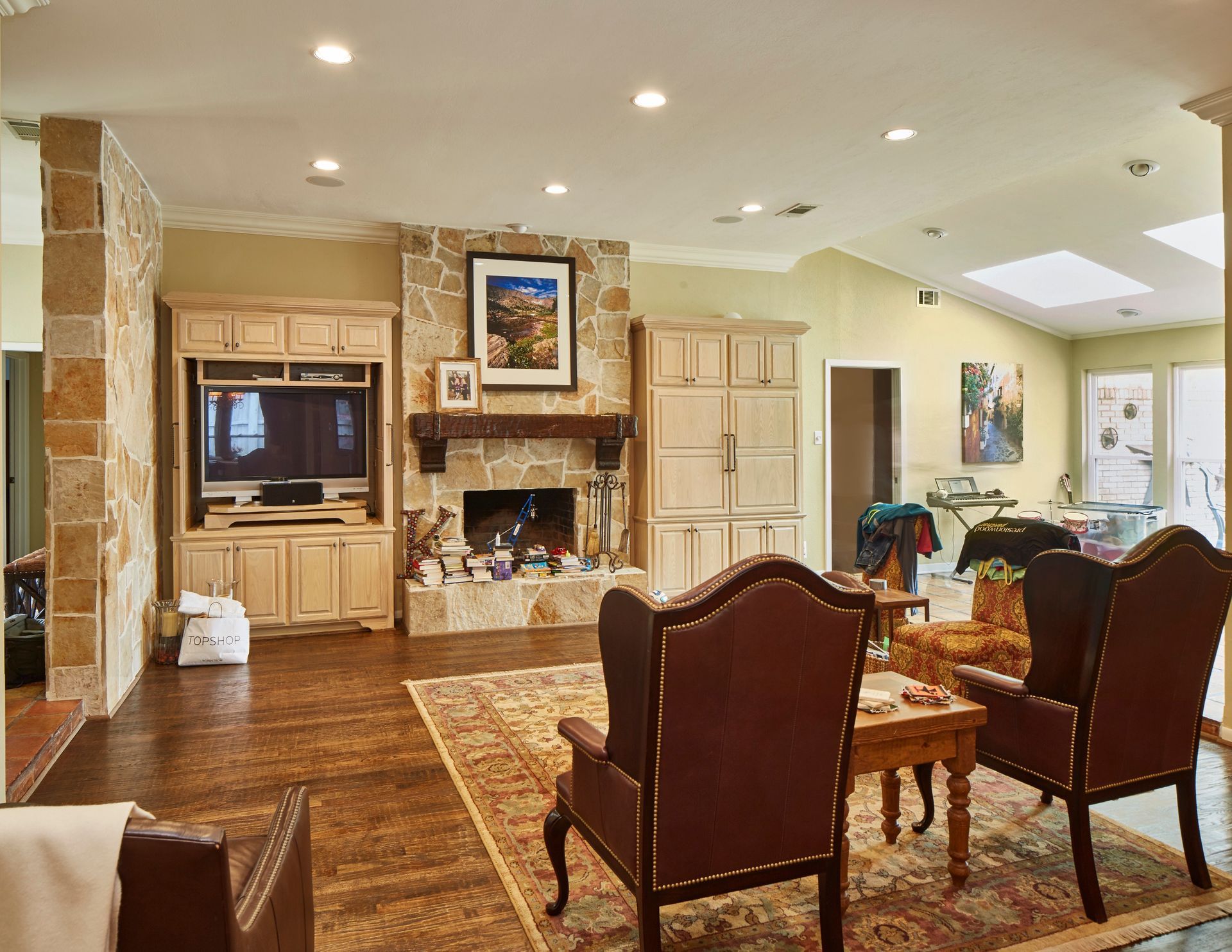 A living room with wooden floors, a stone fireplace, built-in cabinets, two wingback chairs, and an area rug.