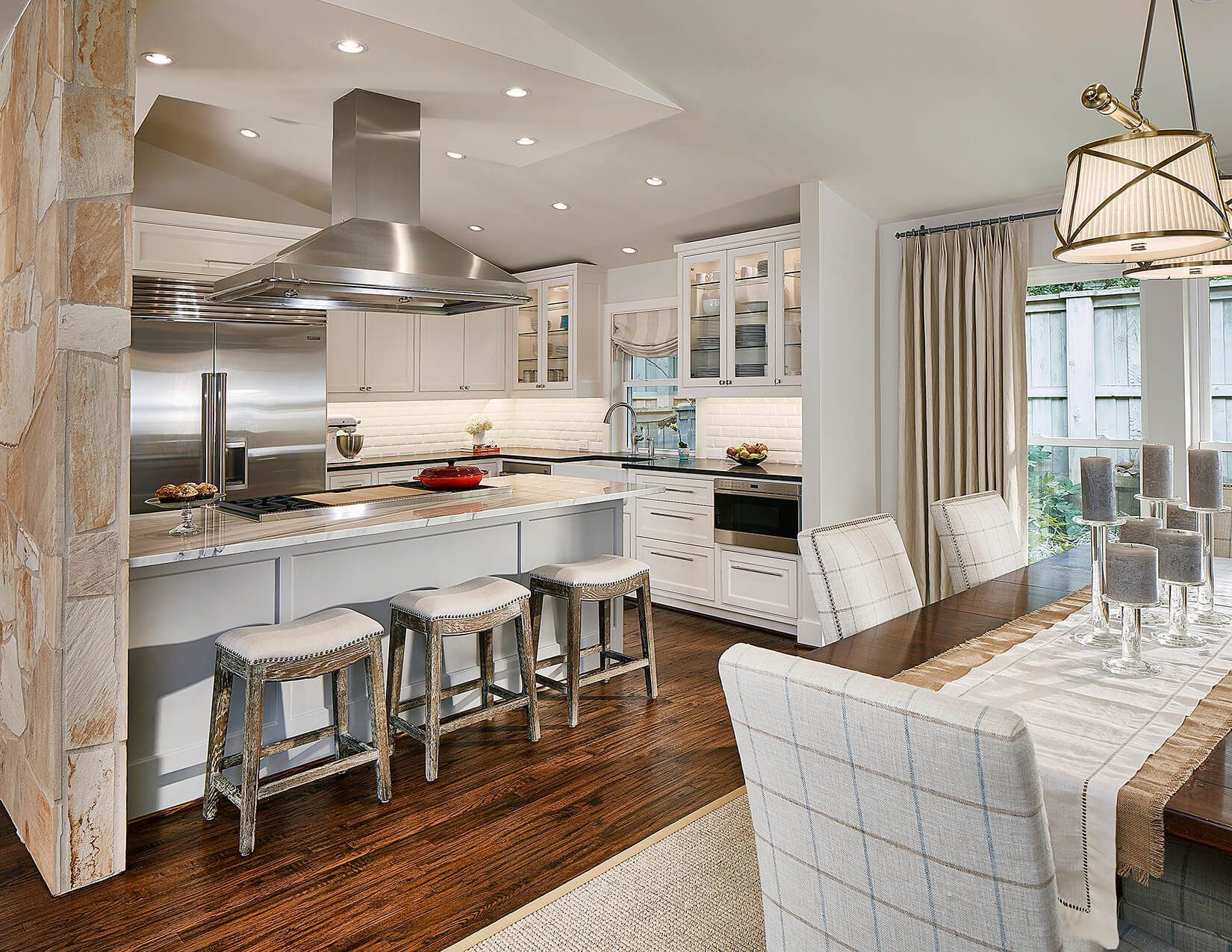 A bright kitchen with white cabinetry, a stone accent wall, a central island with stools, and an adjacent dining area.