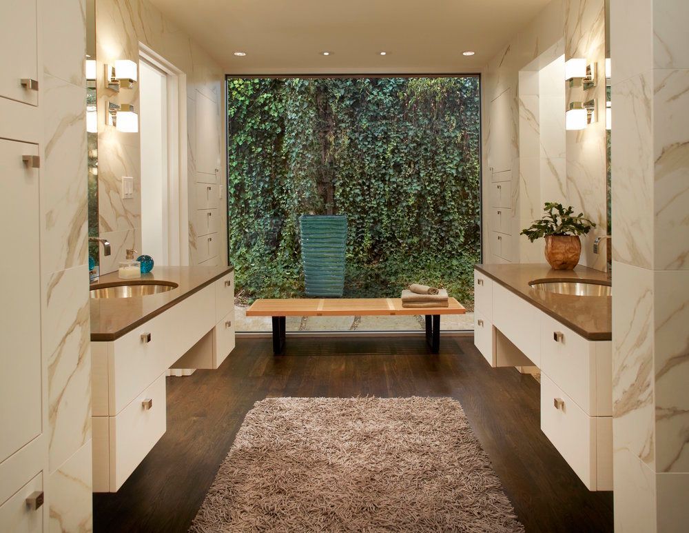 Bathroom with vanity on either side, a large window with greenery, and a shaggy rug.