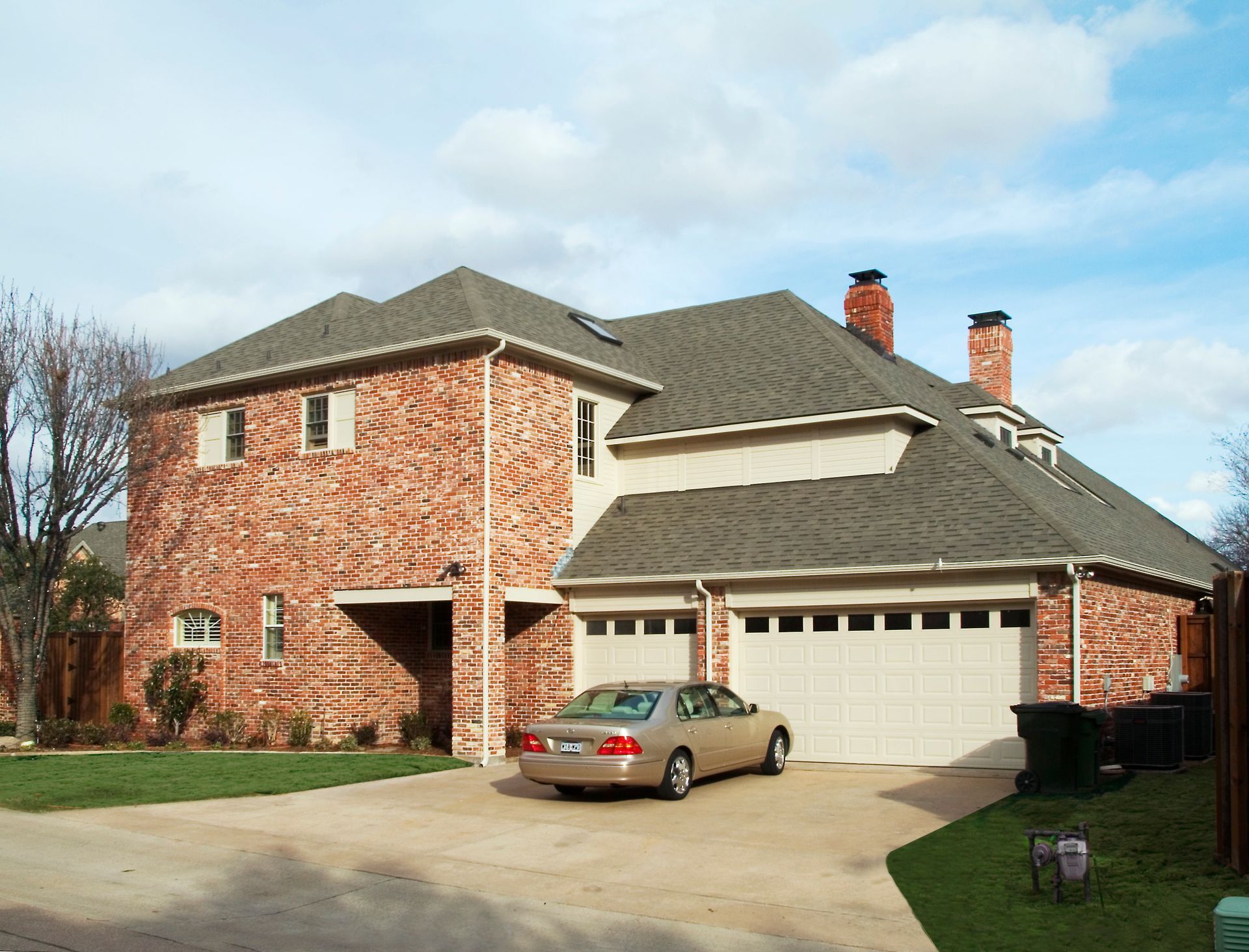 Brick house with two-car garage, sedan parked in front, clear sky.