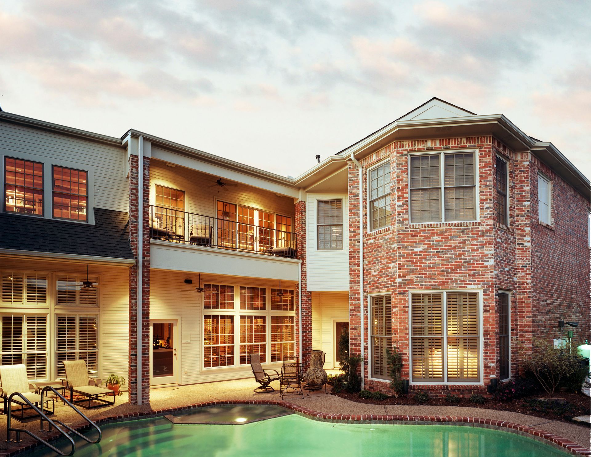 Backyard of a house with a pool. Brick and white siding. Evening light.