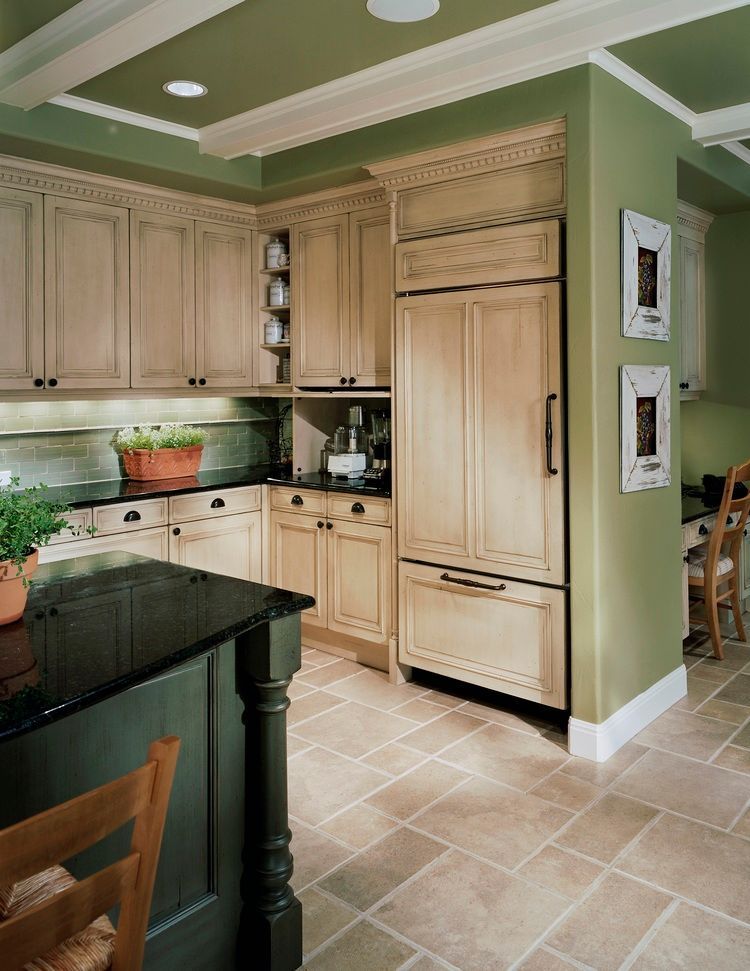Kitchen with light-colored cabinets, black countertops, and green walls. Stone tile floor, and a green island.