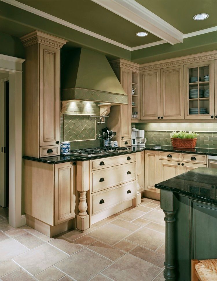 Kitchen with light wood cabinets, black countertops, green walls, and tile flooring.