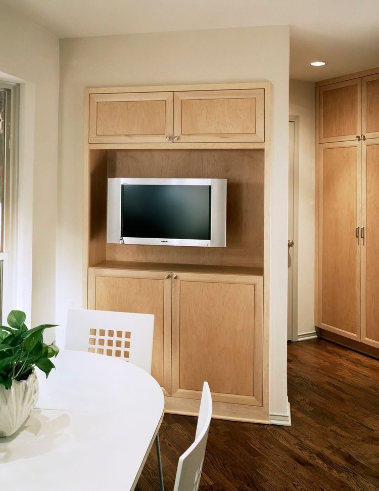 Built-in light wood cabinet with TV, two doors below, two above, white table and chairs in kitchen.