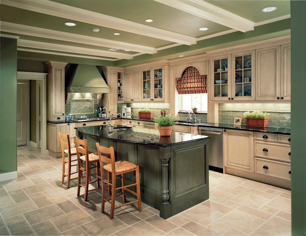 Green and beige kitchen with island, wooden stools, and decorative ceiling beams.