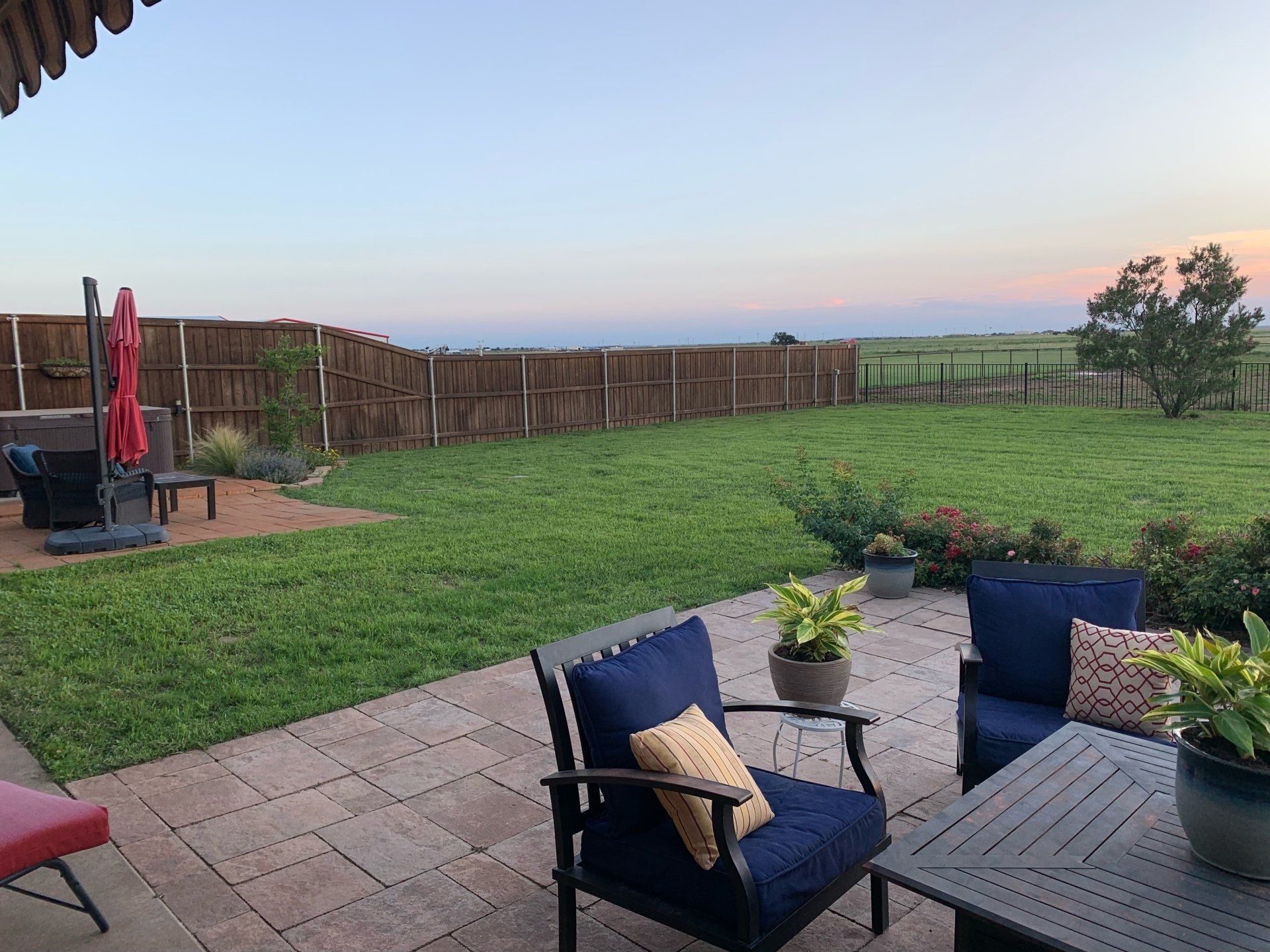 A patio with chairs , a table and a fence in the background.