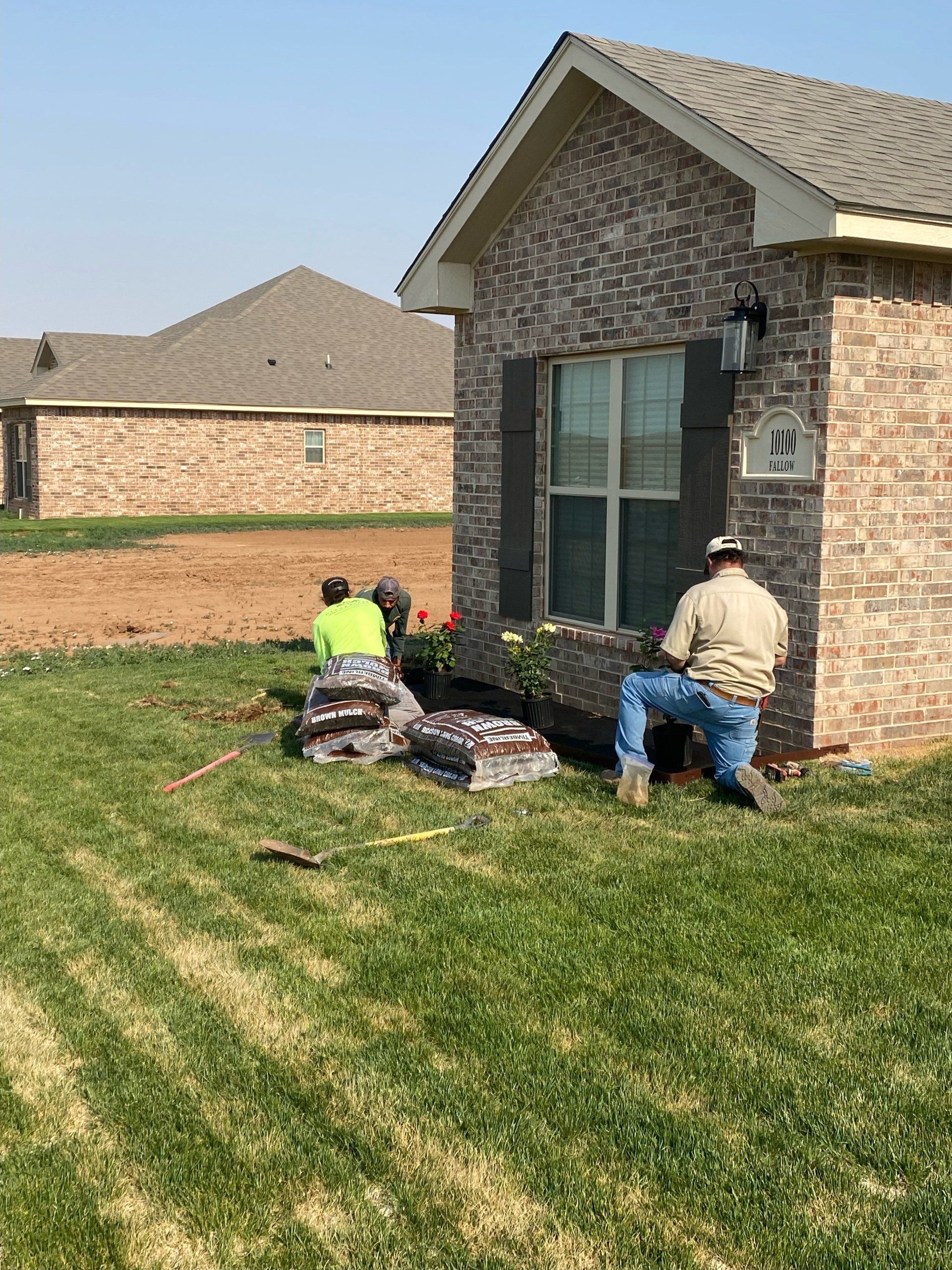 A couple of men are sitting on the grass in front of a brick house.