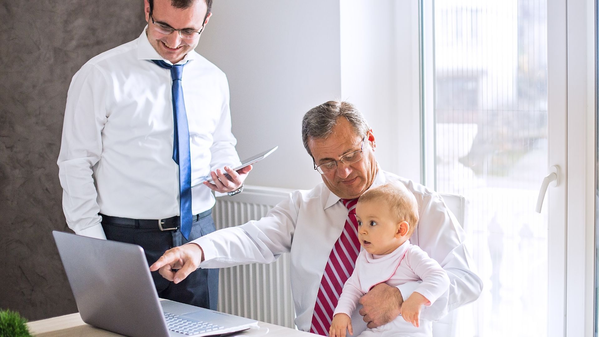 A man is holding a baby while looking at a laptop.