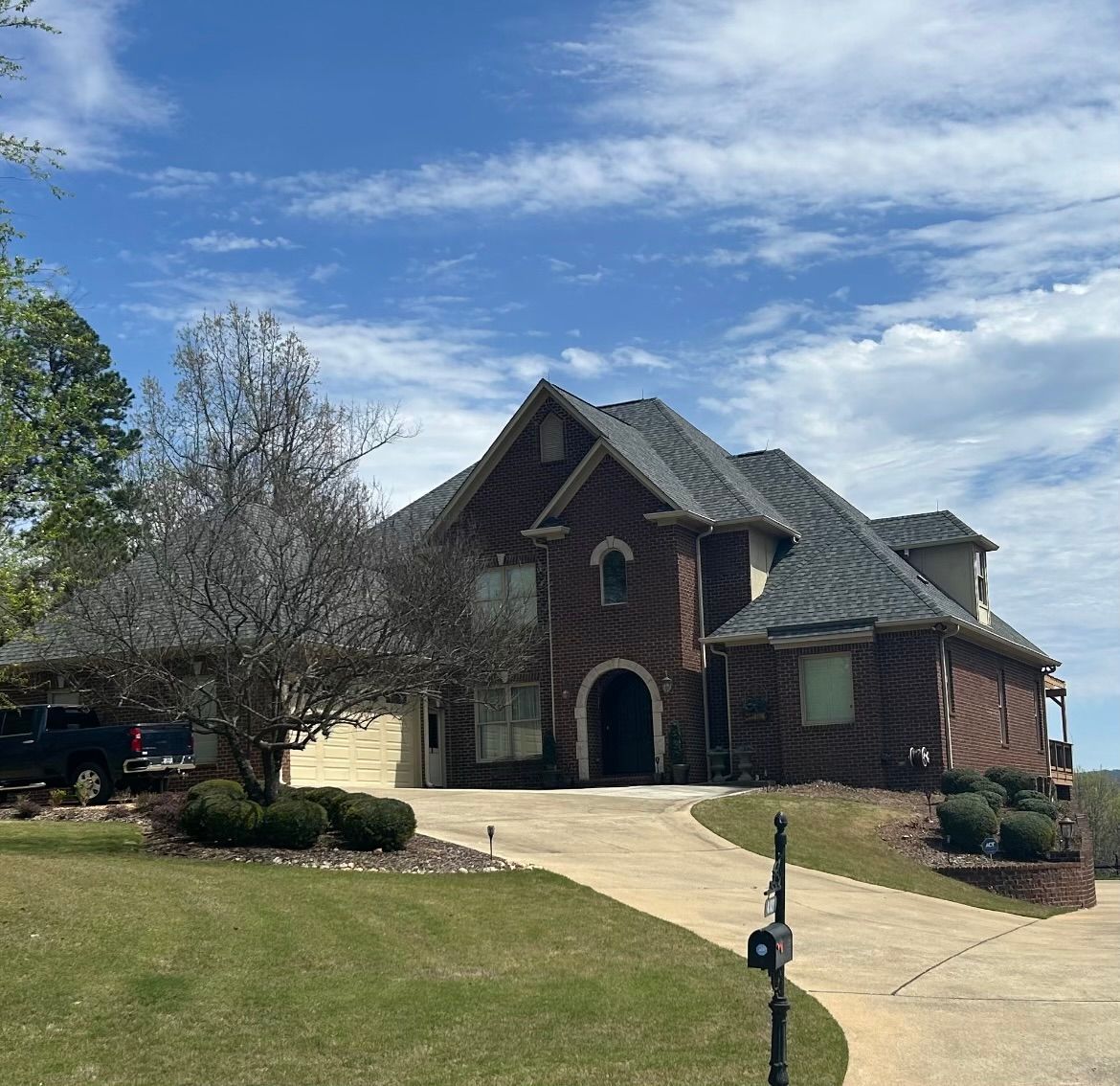 Two-story brick house with a curved driveway on a grassy hill under a blue sky.