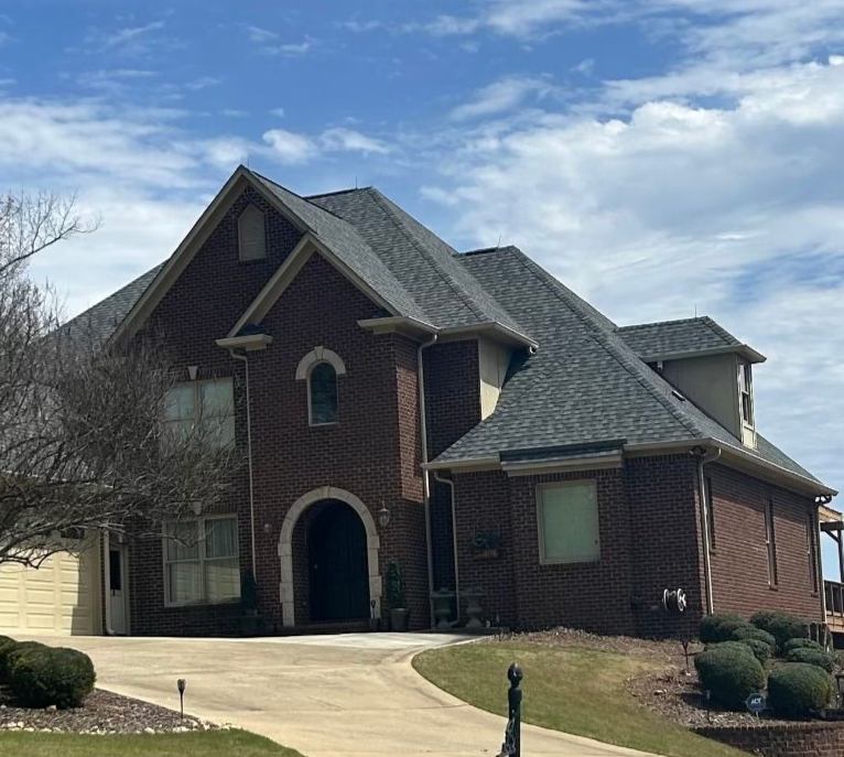 Two-story brick house with a curved driveway on a grassy lawn under a partly cloudy sky.