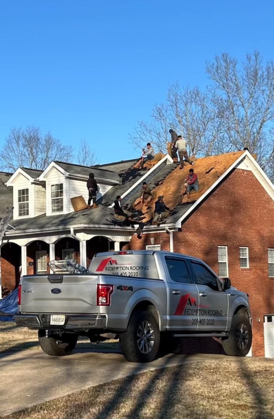 Silver truck parked in front of house. Crew working on roof under clear, blue sky.
