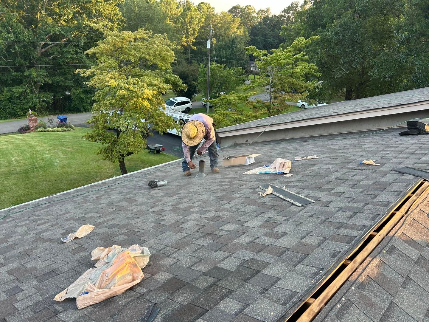 Roofer working on a shingled roof, trees in the background.