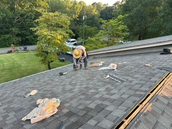 Roofers working on a yellow house, with tarps covering the ground.