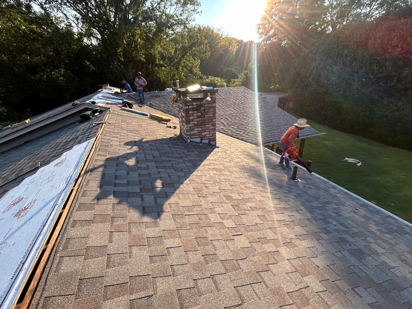 Roofers working on a house roof with a brick chimney in sunlight.