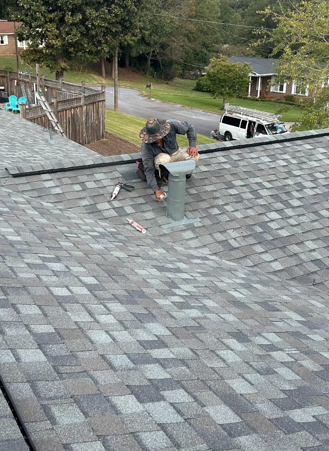 Roofer working on a roof, installing a vent pipe. Outdoors, overcast day, asphalt shingles.
