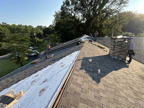 Roofers working on a residential roof, installing shingles and underlayment on a sunny day.