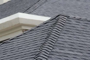 Close-up of a dark gray shingled roof with a white corner of a building.