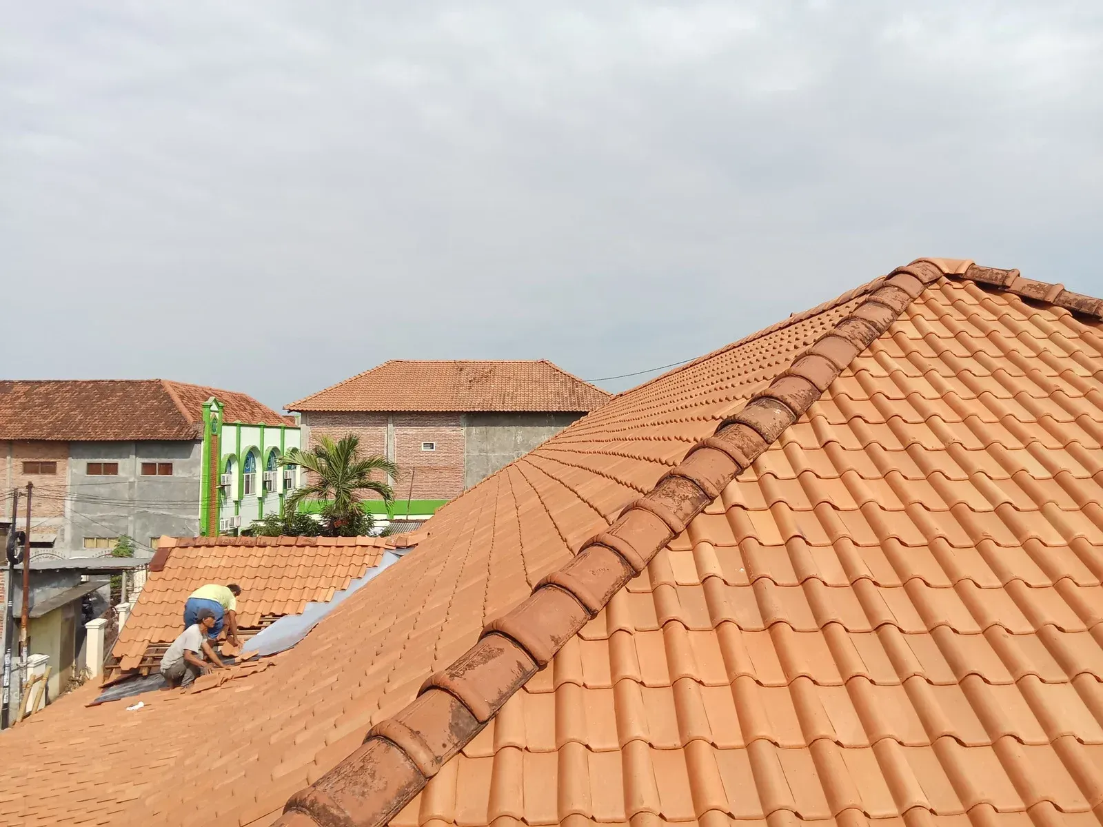 Red tile rooftops with a person working on one under a cloudy sky.
