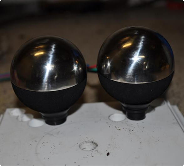 Two polished metal spheres on black bases sit on a white surface.