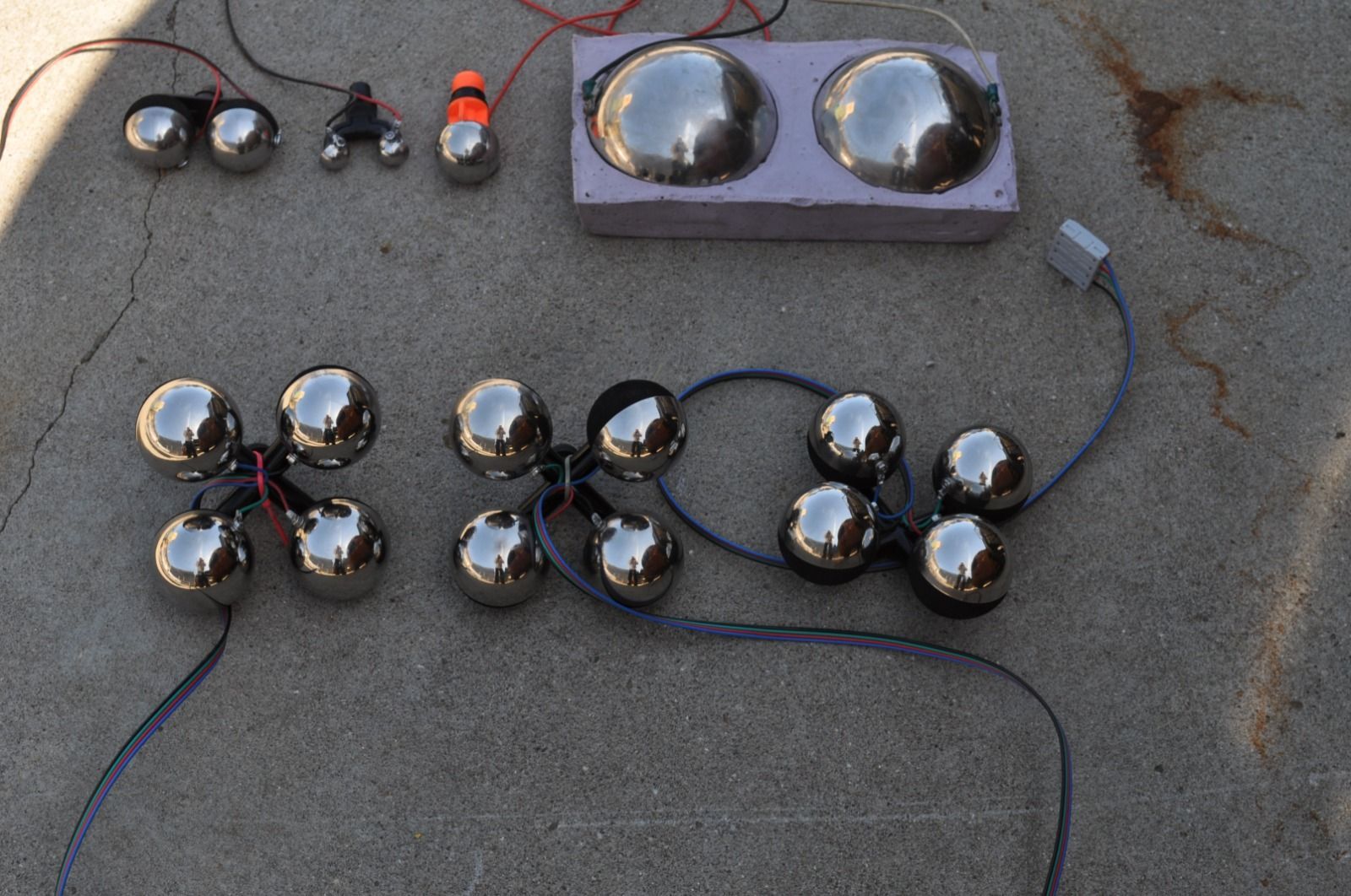 Arrangement of silver spheres connected by wires on concrete. Some spheres are grouped or encased in foam.
