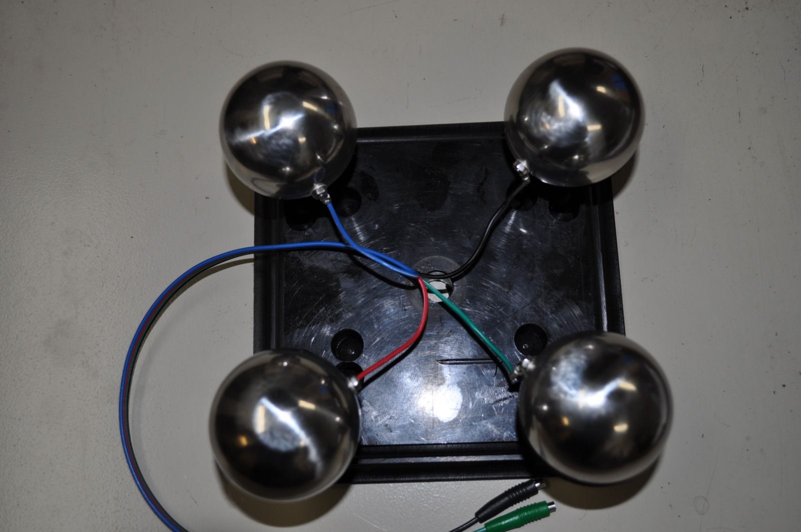 Four silver spheres connected by wires to a central black square.