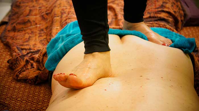 woman massaging man's back with feet