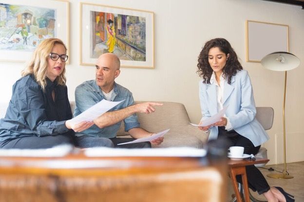 Three people reviewing papers together on a sofa in a bright living room