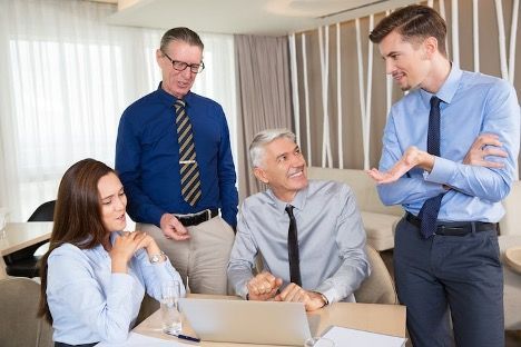 3 men and a woman sitting at a desk, looking at a laptop