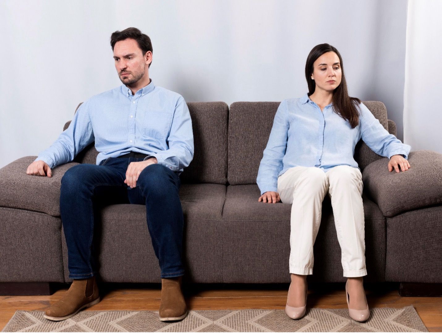 a man and woman sit on a couch, leaning away from each other