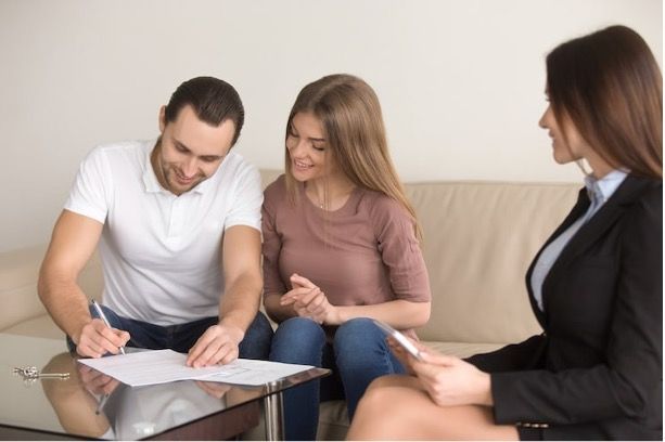 a man and woman sit on a couch signing a document