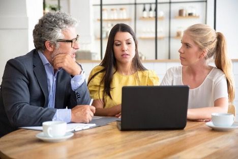 two women and a man sitting at a desk, looking at a laptop