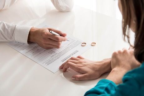 Two people reviewing a document on a desk beside two wedding rings
