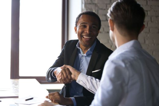 Two men are shaking hands while sitting at a table.