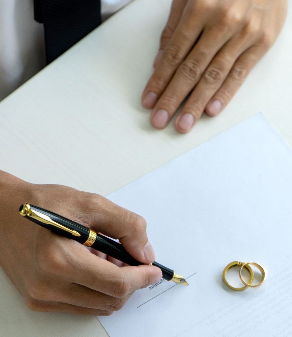 A person is writing on a piece of paper next to a pair of wedding rings.