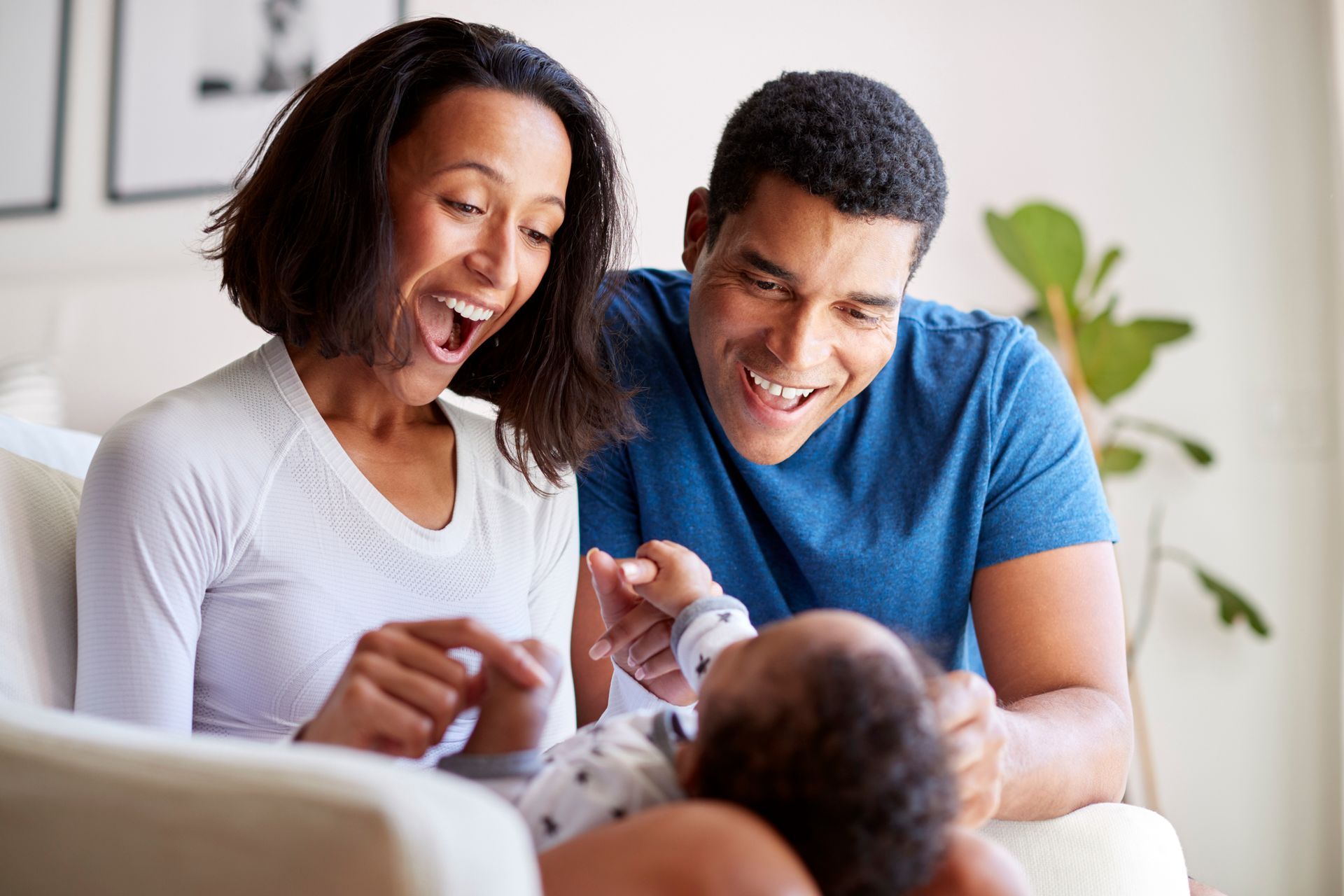 A man and woman are sitting on a couch playing with a baby.