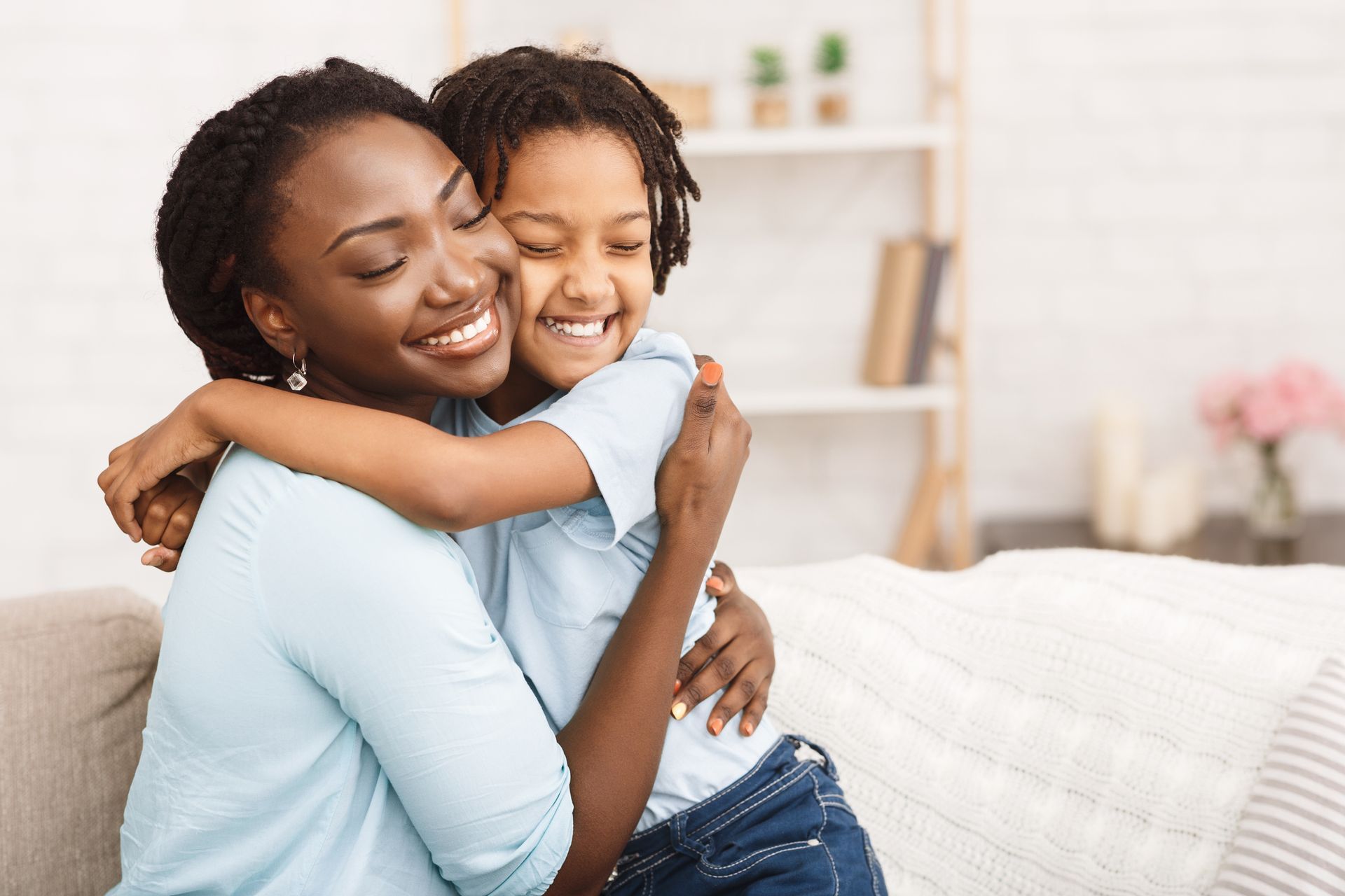 A woman and a child are hugging each other on a couch.