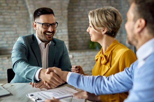 A man and a woman are shaking hands while sitting at a table.