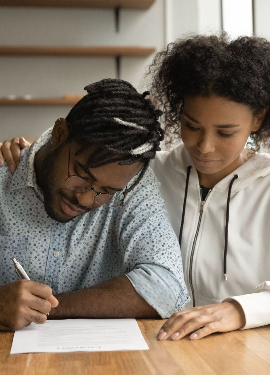 A man and a woman are sitting at a table writing on a piece of paper.